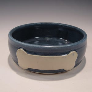 May include: A blue ceramic dog bowl with a white bone design. The bowl is glazed and has a smooth finish.