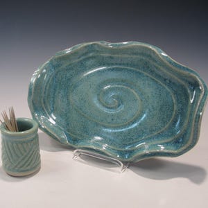 May include: A teal ceramic dish with a swirling design and a matching teal ceramic toothpick holder.