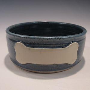 May include: A blue ceramic dog bowl with a white bone design. The bowl is glazed and has a slightly textured surface.