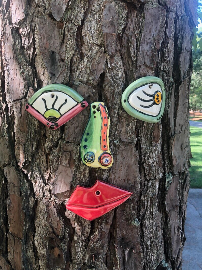 Four pieces which represent a Picasso-Style goofy tree face are placed on a pine tree trunk - two colorful eyes, a nose, and bright red lips.