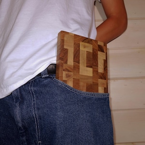 Puede incluir: Una tabla de cortar rectangular de madera con un patrón de mosaico es parcialmente visible en un bolsillo trasero de unos vaqueros azules. La tabla está hecha de varias tonalidades de madera marrón.