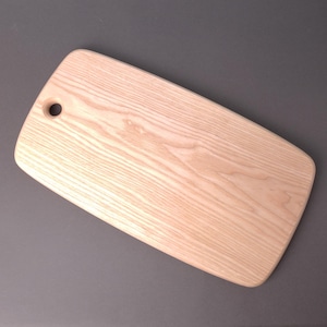 Op de afbeelding: Een rechthoekig houten snijplank met een lichte houtnerf en een klein gat in de linkerbovenhoek.