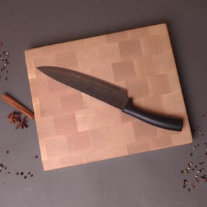 May include: A light wood cutting board with a checkered pattern and a black chef's knife on top.