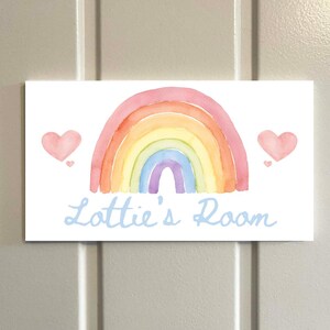 May include: A rectangular sign with a watercolor rainbow design in shades of pink, orange, yellow, green, blue, and purple. Two pink hearts flank the rainbow. The text "Lottie's Room" is written in light blue script.