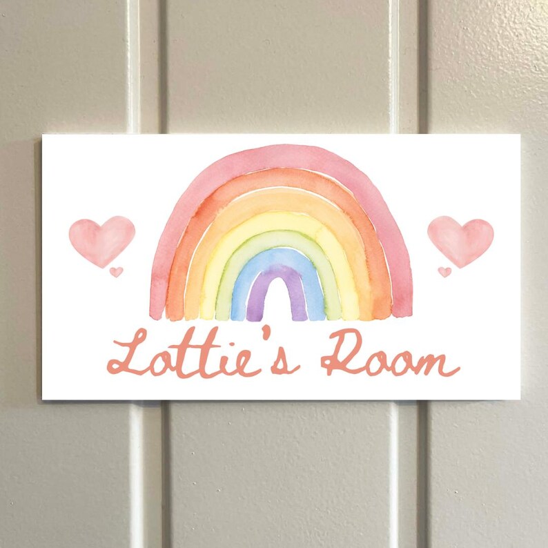 May include: A rectangular sign with a watercolor rainbow design in shades of pink, orange, yellow, green, blue, and purple. Two pink hearts flank the rainbow. The text "Lottie's Room" is written in a cursive font.