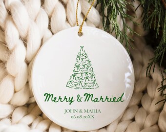 May include: White ceramic Christmas ornament with a green Christmas tree design. The ornament has the text "Merry & Married" and the names "JOHN & MARIA" with a date below. A gold string is attached for hanging.