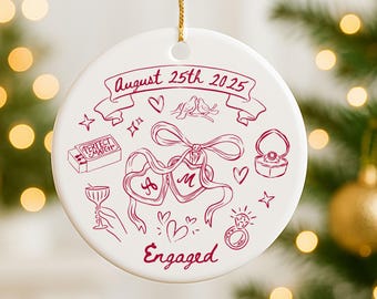 May include: White ceramic ornament with a gold string for hanging. The ornament features a hand-drawn design in burgundy, including hearts, rings, and the text "August 25th 2025" and "Engaged".