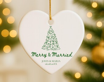May include: A heart-shaped, white ceramic Christmas ornament with a green Christmas tree design. The ornament has the text "Merry & Married" and the names "JOHN & MARIA" with a date. A gold string is attached for hanging.