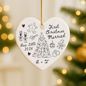 May include: A heart-shaped, white ceramic Christmas ornament with a gold string. The ornament features black line drawings of a Christmas tree, champagne glasses, and a gingerbread man. Text reads "First Christmas Married" and "Aug 25th 2025".
