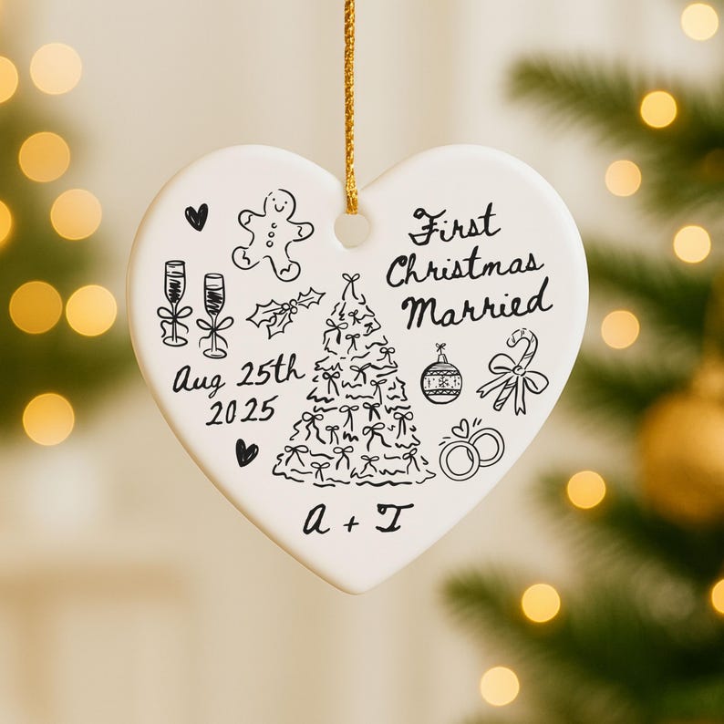 May include: A heart-shaped, white ceramic Christmas ornament with a gold string. The ornament features black line drawings of a Christmas tree, champagne glasses, and a gingerbread man. Text reads "First Christmas Married" and "Aug 25th 2025".