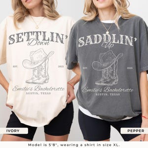 May include: Two oversized t-shirts, one ivory and one pepper, feature a cowboy hat and boot graphic with the text "Settlin' Down" and "Saddlin' Up". The shirts also include "Emilie's Bachelorette, Austin, Texas" and the year 2025.