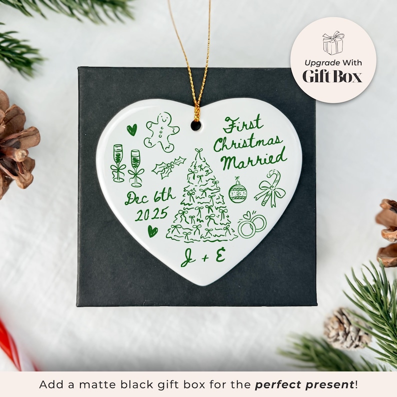 May include: A white heart-shaped Christmas ornament with green illustrations and text, including "First Christmas Married" and "Dec 6th 2025." The ornament is in a black gift box, with a gold string for hanging.