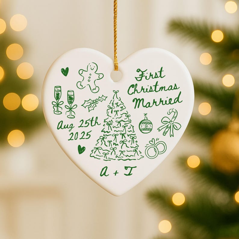 May include: A heart-shaped, white ceramic Christmas ornament with green illustrations and text. The ornament features a Christmas tree, champagne glasses, and the words "First Christmas Married" and "Aug 25th 2025". A gold string is attached for hanging.