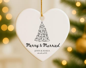May include: A heart-shaped, white ceramic Christmas ornament with a gold string. The ornament features a black illustration of a Christmas tree and the text "Merry & Married" with a couple's names and date.