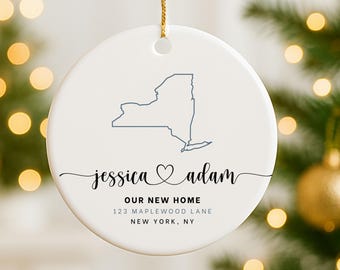 May include: White ceramic ornament with a gold string for hanging. The ornament features a blue outline of the New York state map, the names "jessica & adam", and the text "OUR NEW HOME" with an address below.