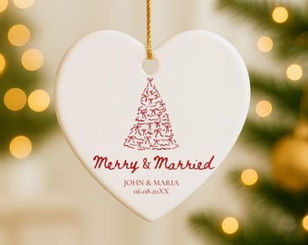 May include: A heart-shaped, white ceramic Christmas ornament with a red Christmas tree design. The ornament has the words "Merry & Married" and the names "John & Maria" with a date printed in red.