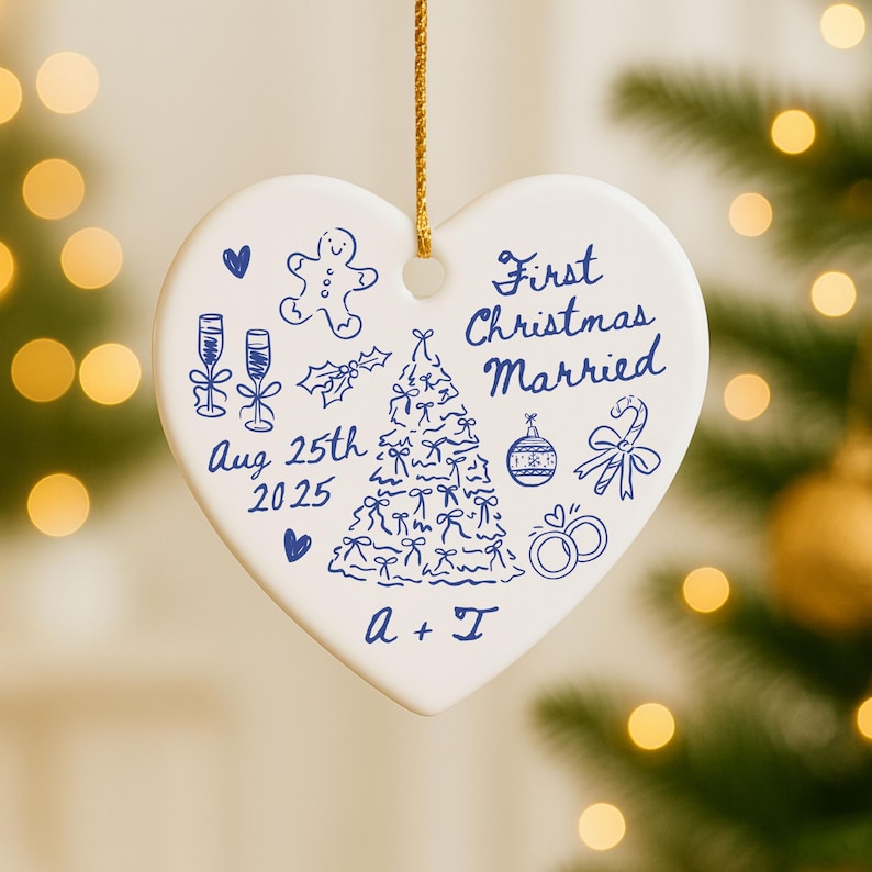 May include: A white heart-shaped Christmas ornament with blue illustrations and text. The ornament features a Christmas tree, champagne glasses, and the words "First Christmas Married" and "Aug 25th 2025". A gold string is attached for hanging.