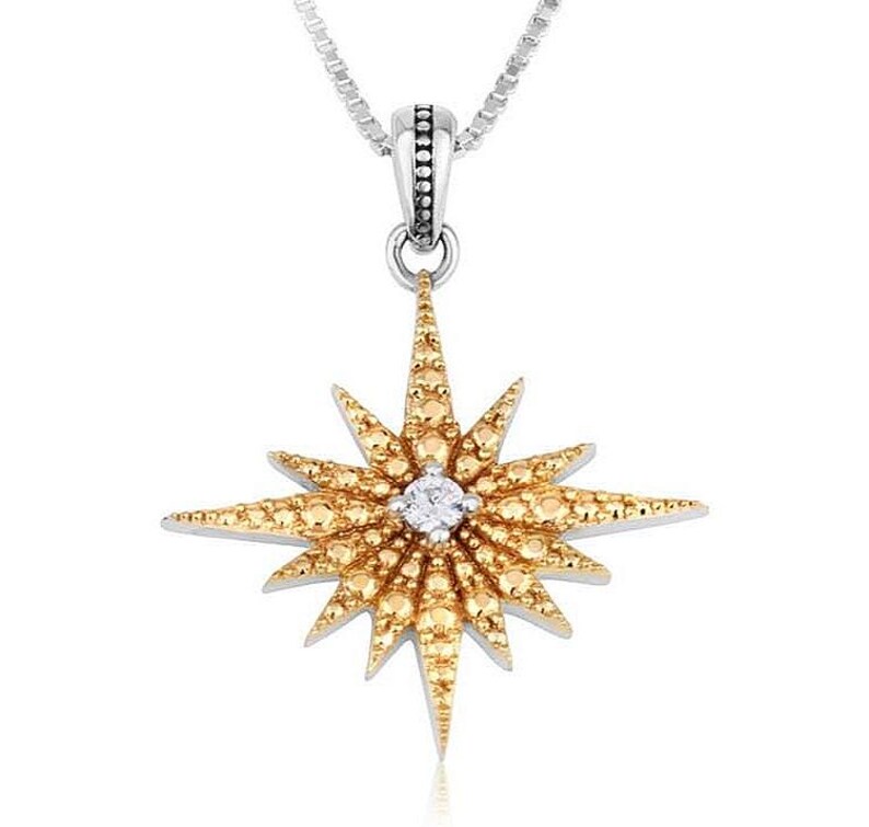 May include: A silver necklace with a pendant shaped like a golden starburst. The starburst is studded with small, yellow-gold gems and a single, clear gem in the center. The necklace chain is a delicate silver.