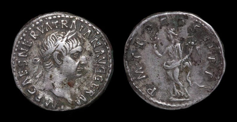 May include: Two silver Roman coins. One coin features a profile of a man with text around the edge. The other coin shows a standing figure with text. Both coins are against a black background.