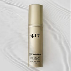May include: A gold-coloured facial serum bottle with the text "-417" in black. The bottle also features the words "TIME CONTROL", "MULTI-ACTIVE FACIAL SERUM", and "Serum actif contre les rides". The background is a light, wavy pattern.