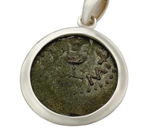 May include: A silver pendant featuring an ancient coin. The coin has a dark green patina and visible markings. The pendant has a simple, polished silver bezel and a loop for a chain.