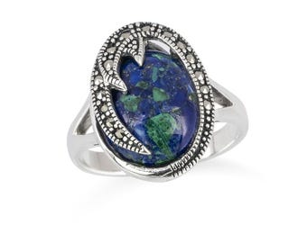 May include: A silver ring featuring an oval-shaped, blue and green stone. The stone is set within a decorative frame of smaller, silver-colored stones. The ring has a split shank design.