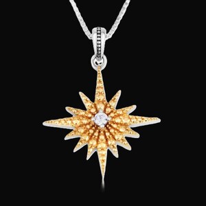 May include: A gold-colored starburst pendant necklace with a silver chain. The starburst has a central clear stone and is surrounded by smaller, yellow-toned stones. The background is black.