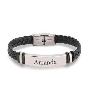 May include: Black braided leather bracelet with a silver-tone plate engraved with the name "Amanda". The bracelet features a stainless steel clasp and silver accents.