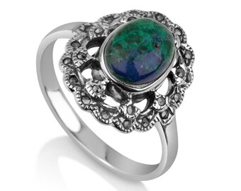 May include: A silver ring featuring an oval-shaped, blue-green gemstone. The gemstone is set within a decorative, openwork setting with small, dark accents. The ring has a polished, smooth band.