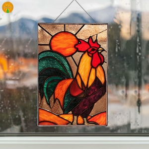 Peut inclure: Panneau en vitrail représentant un coq aux couleurs vives, avec une crête et des barbillons rouges, un corps jaune et orange et des plumes de queue vertes. Le coq se détache sur un soleil orange et un fond brun texturé. Le panneau est suspendu par une chaîne.