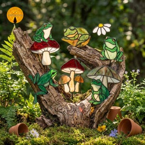 May include: A collection of stained glass garden stakes featuring green frogs, red and white mushrooms, and a white daisy. The frogs are depicted in various poses, including sitting on mushrooms, resting on leaves, and holding a mushroom umbrella.