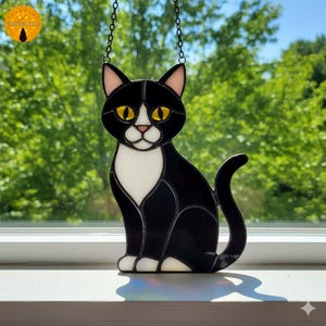 May include: A black and white stained glass cat with yellow eyes and pink ears, suspended by a chain. The cat is depicted in a seated position. The background shows blurred green trees.