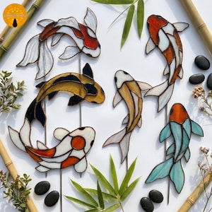 Peut inclure: Cinq ornements de poissons koï en vitrail de différentes couleurs, notamment orange, blanc, jaune, noir et bleu clair. Chaque poisson est construit avec des lignes de métal soudées et fixé sur une fine tige métallique pour le jardin.