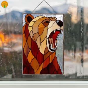 May include: A rectangular stained glass panel showing a roaring bear. The bear's head is made up of brown, amber, and red glass pieces, with a white snout and open mouth. The panel is suspended by a chain, suitable for hanging.