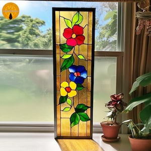 May include: A stained glass panel with a floral design. It features red, blue, and yellow flowers, green leaves, and a gold background. The rectangular panel is framed in black, suitable for window or wall decor.