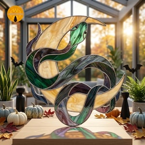 Pode incluir: Uma escultura de vitral de uma cobra enrolada com painéis de vidro translúcido nas cores verde, roxo escuro e creme, unidos por soldas de metal escuro. A cobra está posicionada em uma forma sinuosa sobre uma base de madeira plana.