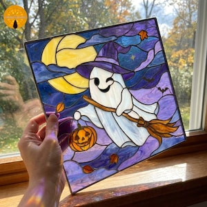 May include: Stained glass Halloween panel featuring a winking ghost in a witch hat, flying on a broom. The artwork includes a jack-o'-lantern, a full moon, and bats against a purple and blue night sky. The panel is square and has a metal hanging loop.
