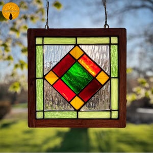 May include: Stained glass window panel with a geometric design. The panel features a central diamond shape in red and green, surrounded by yellow and green squares, set within a dark brown wooden frame. The glass has a textured appearance.