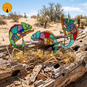 May include: Three stained glass chameleon figures featuring multicoloured geometric panels in shades of green, blue, purple, red, and yellow. Each chameleon is mounted on a thin black metal stake, showcasing intricate leaded glass construction.
