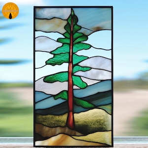 May include: Stained glass panel depicting an evergreen tree with a red trunk and green foliage. The background shows a landscape with white and blue mountains and a light blue sky. The panel is framed in black.