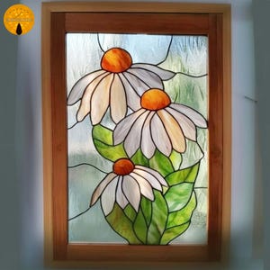 May include: A stained glass panel depicting three large daisies. The flowers have white petals and orange centres, set against a light blue background with green leaves. The panel is framed in natural wood.