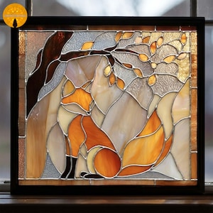 Puede incluir: Panel de vidrieras que representa un zorro sentado bajo un árbol con hojas de otoño. La obra de arte utiliza tonos de naranja, marrón y crema, con un marco negro. El zorro tiene una cola esponjosa y está situado contra un telón de fondo montañoso.
