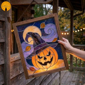 May include: A framed stained glass panel depicting a jack-o'-lantern wearing a witch's hat, set against a full moon and swirling purple and blue patterns. The panel is lit, producing a warm light. The frame is wooden.