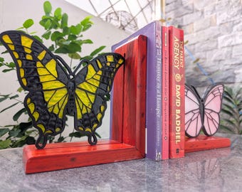 May include: Red wooden bookends with butterfly designs. One butterfly is black and yellow, the other is pink. Books with titles like "The Parent Agency" and "Hamster in a Hamper" are held between the bookends.