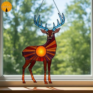 May include: Stained glass deer suncatcher with a brown body, blue antlers, and a sunburst design in shades of orange and purple. The suncatcher hangs from a chain and is displayed in front of a window.