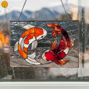 Pode incluir: Painel de vitral com dois peixes koi em tons de laranja, vermelho, branco e prata. Os peixes estão dispostos em um design yin-yang, em um fundo aquoso texturizado. O painel é emoldurado em metal escuro e suspenso por uma corrente.