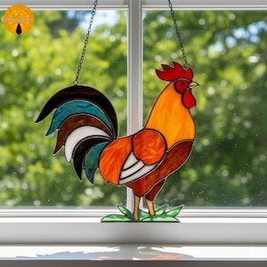 以下が含まれることがあります： 鮮やかなデザインのステンドグラスの雄鶏。雄鶏は赤い鶏冠、オレンジ色の体、青、茶色、白の色合いのマルチカラーの尾が特徴です。チェーンから吊り下げられており、窓の装飾に最適です。