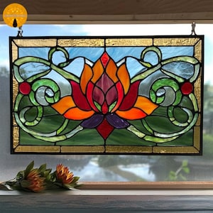 May include: Stained glass panel featuring a lotus flower design. The flower has red, orange, and purple petals, surrounded by green and blue accents. The panel is framed with a gold border and is hanging in front of a window.