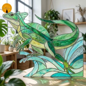 Peut inclure: Un panneau en vitrail représentant un lézard basilic vert courant sur l'eau. Le lézard présente diverses nuances de verre vert et jaune, tandis que l'eau est rendue en verre bleu clair, sarcelle et blanc avec des lignes de soudure en métal sombre.