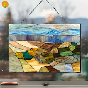 May include: Stained glass panel depicting a landscape scene with rolling hills and mountains. The artwork features a variety of colors, including blues, greens, browns, and yellows, and is framed with a black border. The panel is suspended by a chain.